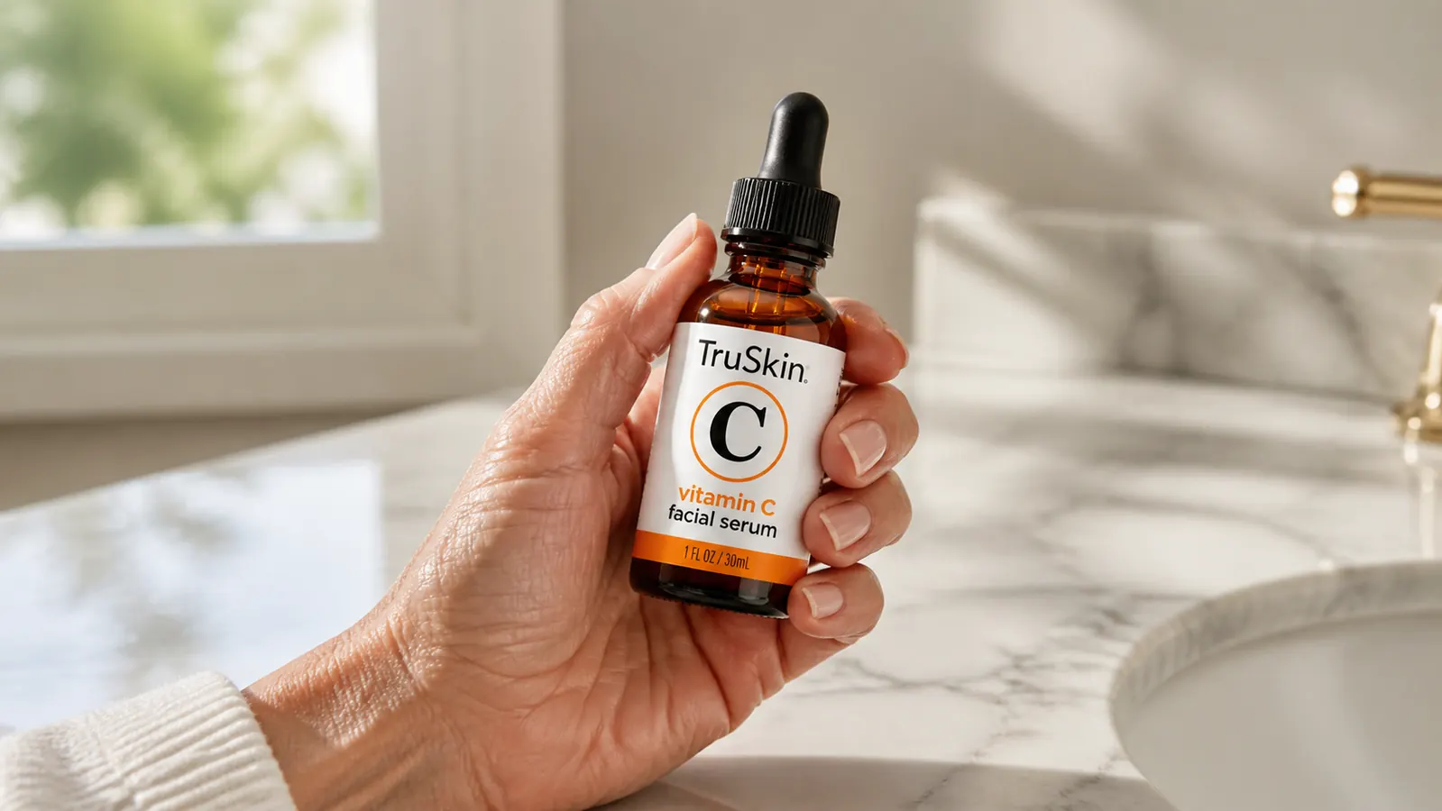 Close-up of a dropper bottle of TruSkin Vitamin C Serum held in a woman's hand over a marble counter