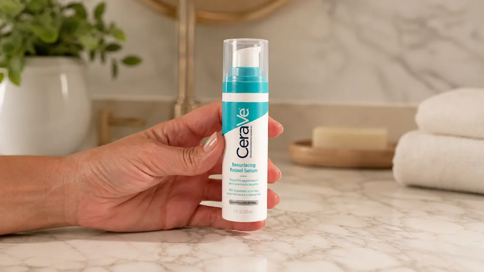 Close-up of a hand holding the CeraVe Resurfacing Retinol Serum bottle against a marble bathroom counter