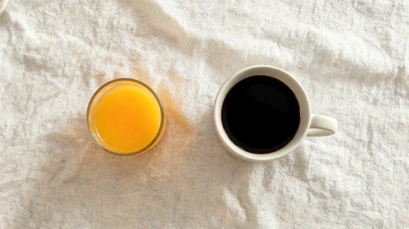 A small glass of orange juice and a mug of coffee side by side on a linen place mat, representing the vitamin C pairing approach