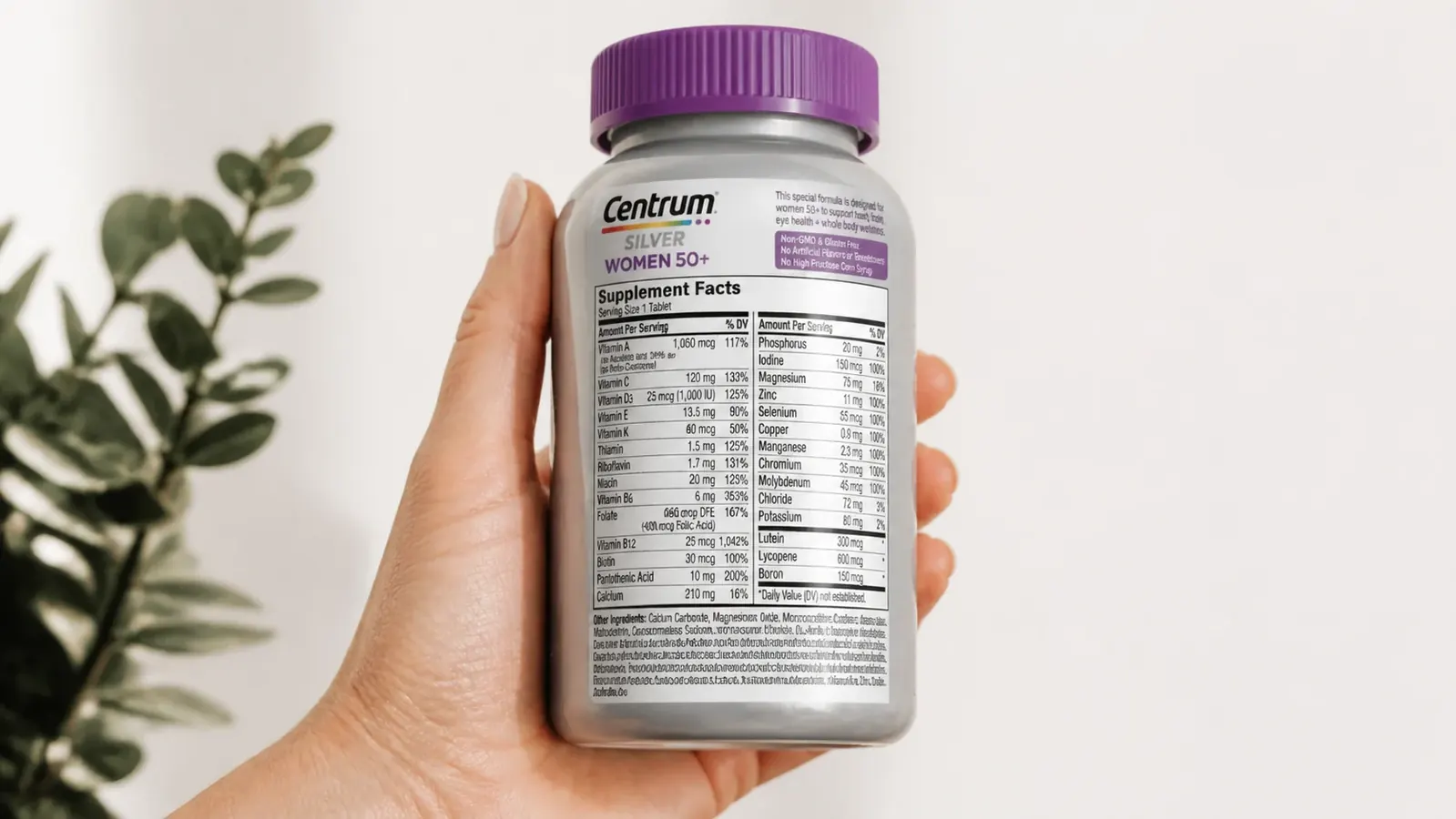 Close-up of a hand holding a Centrum Silver Women 50+ bottle, back label visible with supplement facts panel