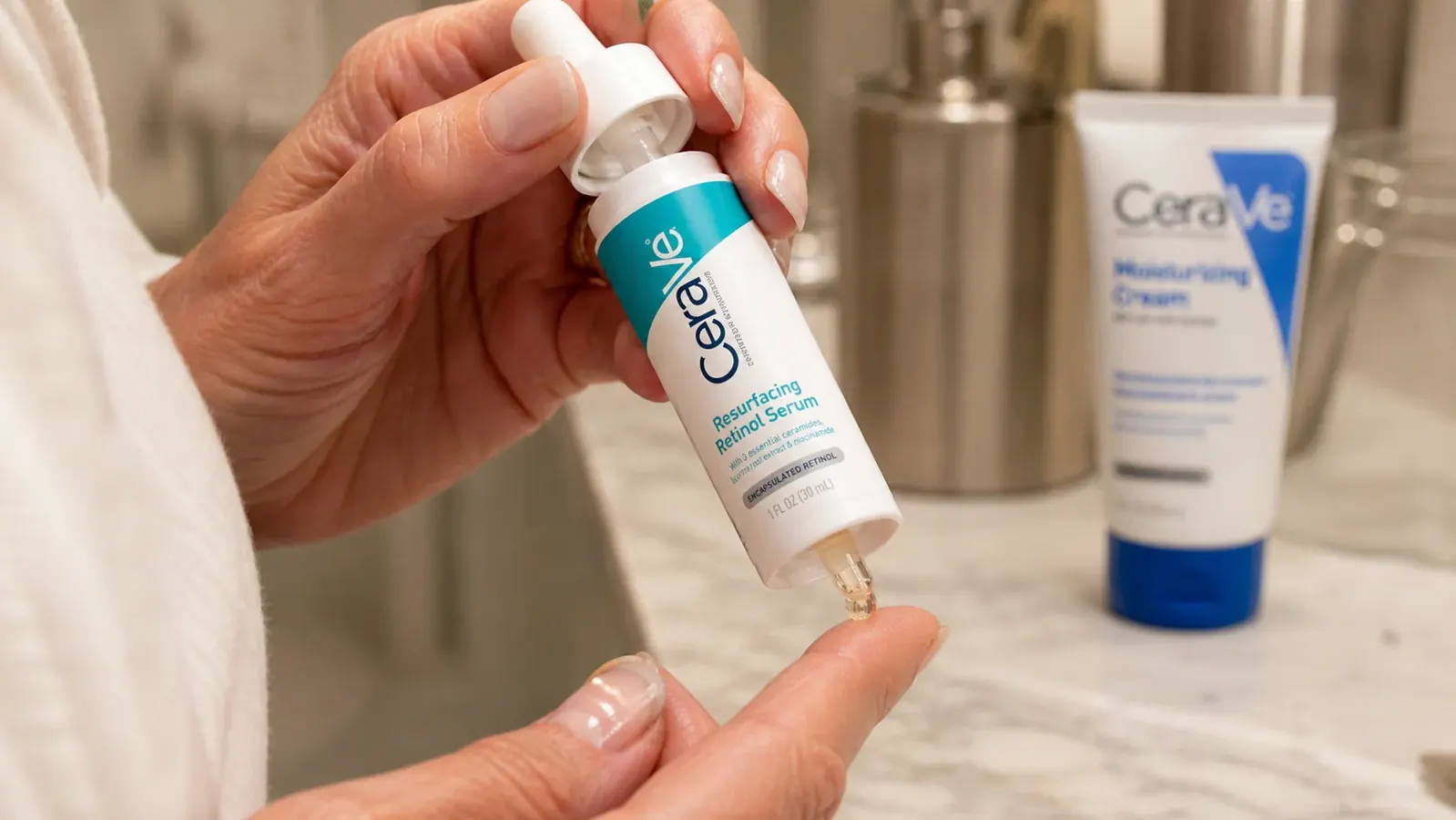 Close-up of hand dispensing CeraVe Resurfacing Retinol Serum onto fingertip next to a moisturizer bottle