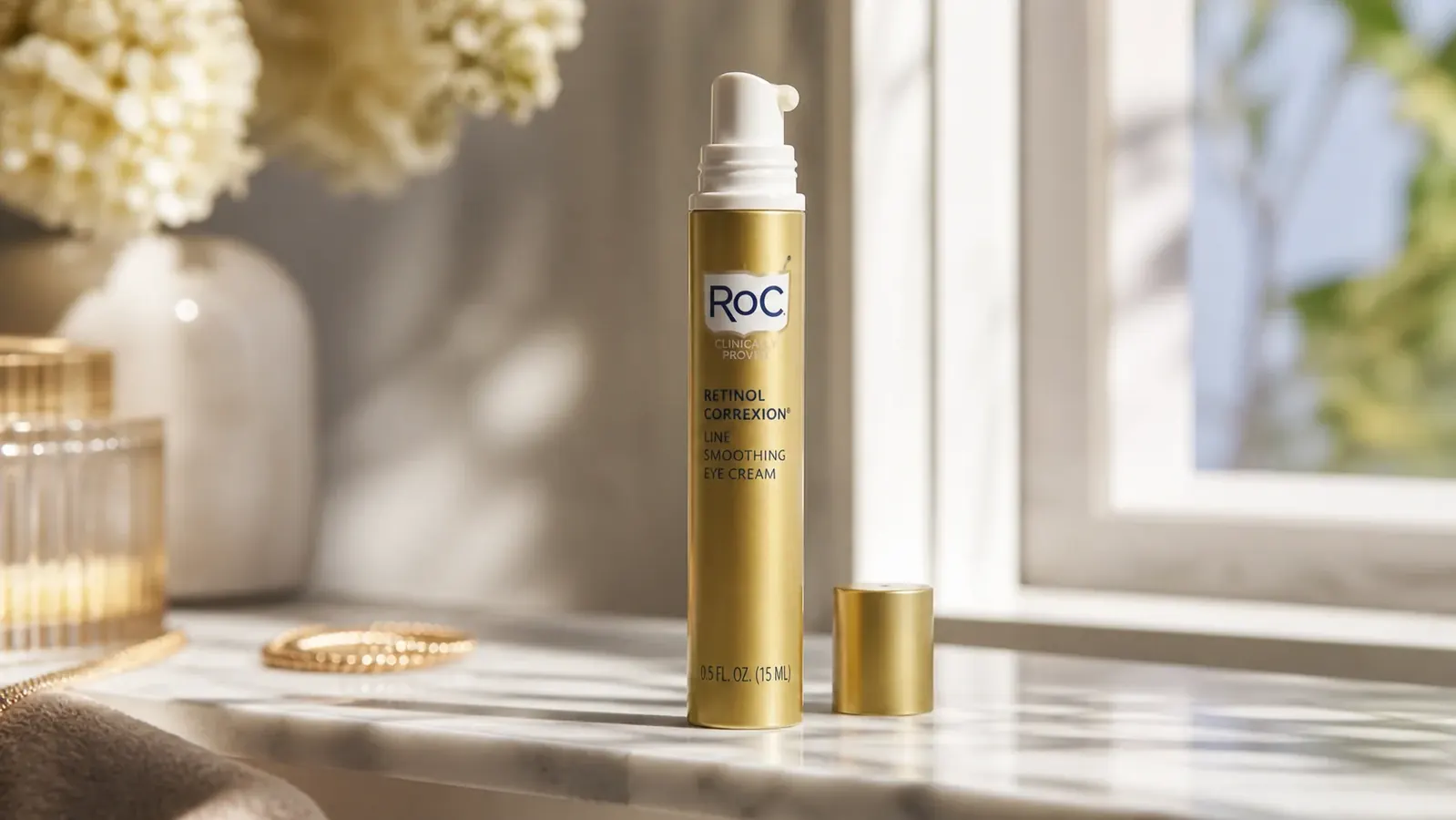 Close-up of the RoC Retinol Correxion Under Eye Cream airless pump tube on a marble bathroom shelf with the small dispensed amount visible on the pump head